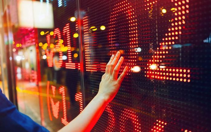 Woman's hand on stock exchange market display screen board on the street showing stock drops in red colour